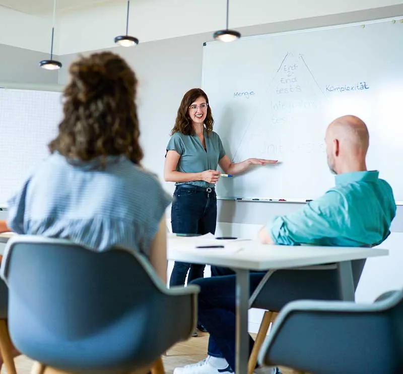 Mitarbeitende besprechen sich vor einem Whiteboard.